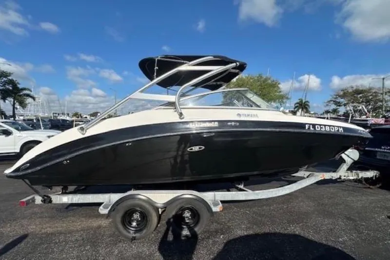 The Image of 2012 Yamaha Boats 242 Limited S on trailer, black and white design, parked outdoors. - 0