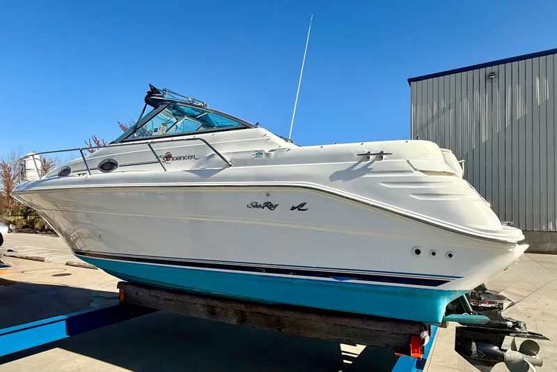 Slide: The Image of 1997 Sea Ray 270 Sundancer boat on trailer, white hull, blue accents, clear sky background. - 10