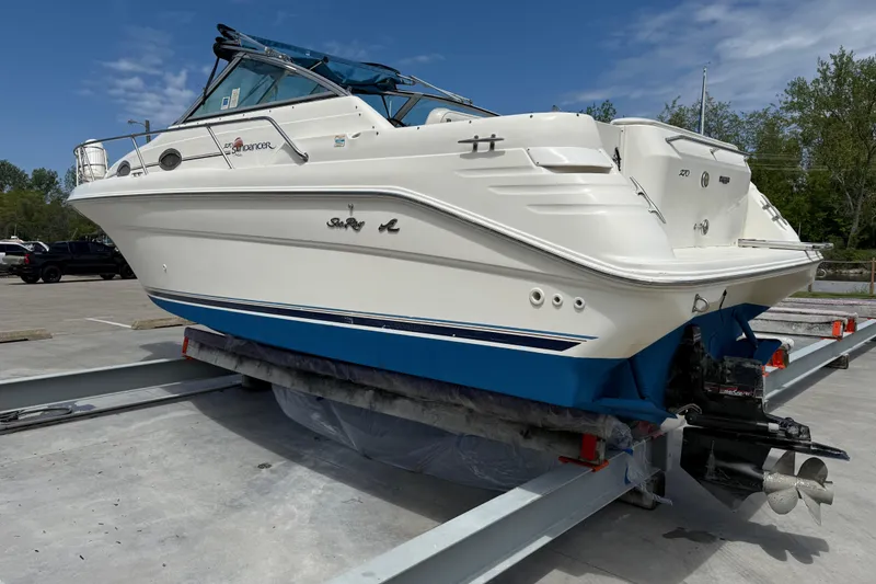 Slide: The Image of 1997 Sea Ray 270 Sundancer boat on trailer, white hull with blue accents, parked outdoors. - 2