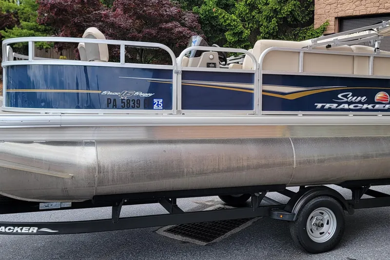 The Image of 2024 Sun Tracker Bass Buggy 16 XL Select pontoon boat on trailer, parked outdoors. - 1