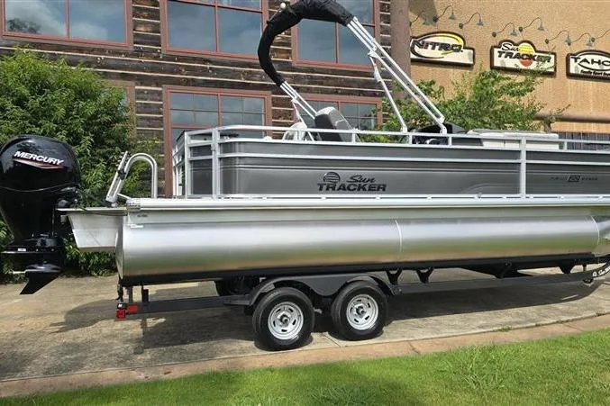 Slide: The Image of 2026 Sun Tracker Fishin' Barge 22 DLX pontoon boat on trailer, parked outdoors. - 2
