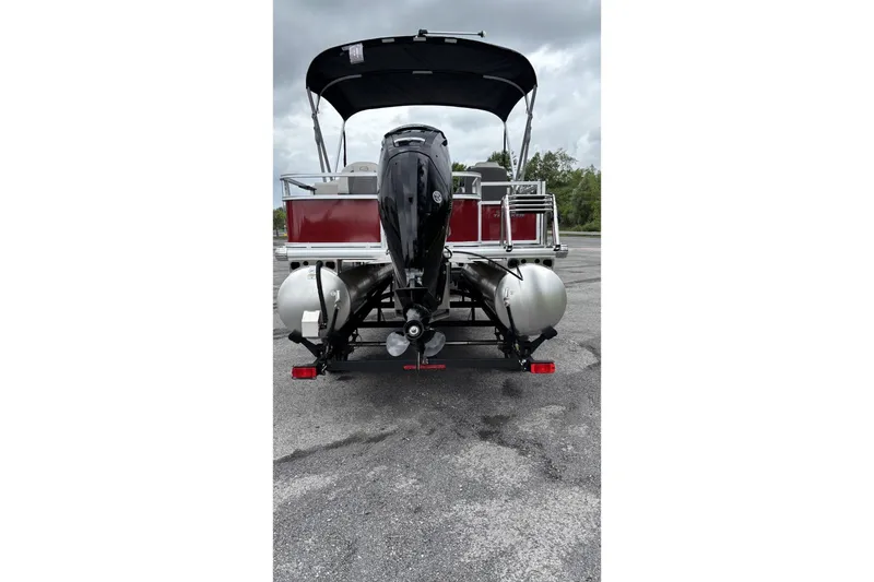 Slide: The Image of 2026 Sun Tracker Bass Buggy 18 DLX pontoon boat, rear view with motor, parked outdoors. - 2