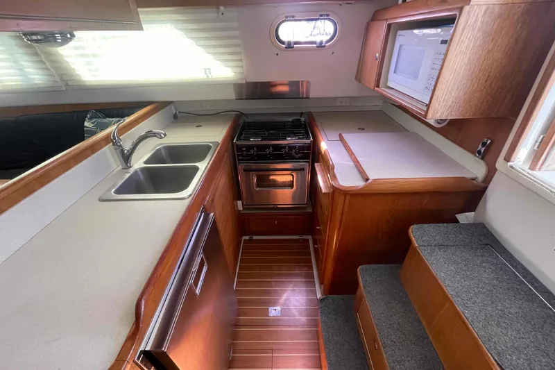 Slide: The Image of 2013 Catalina Morgan 440 yacht kitchen with stove, sink, and microwave in wooden cabinetry. - 3