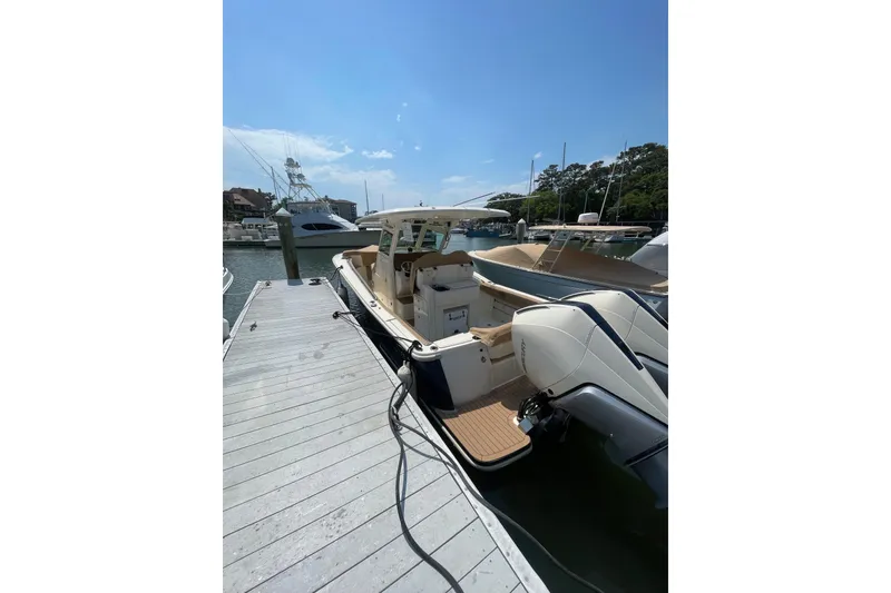 Slide: The Image of 2023 Scout 305 LXF boat docked at marina under clear blue sky. - 1