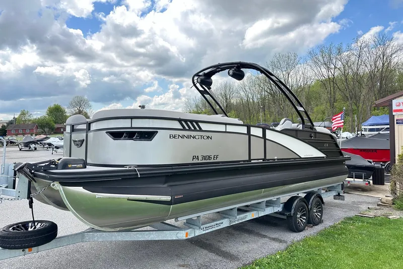 Slide: The Image of 2024 Bennington LX Sport Line pontoon boat on trailer, parked outdoors under cloudy sky. - 12
