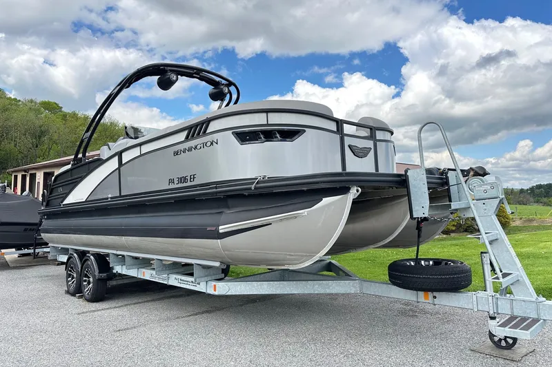 Slide: The Image of 2024 Bennington LX Sport Line pontoon boat on trailer, parked outdoors under a cloudy sky. - 13