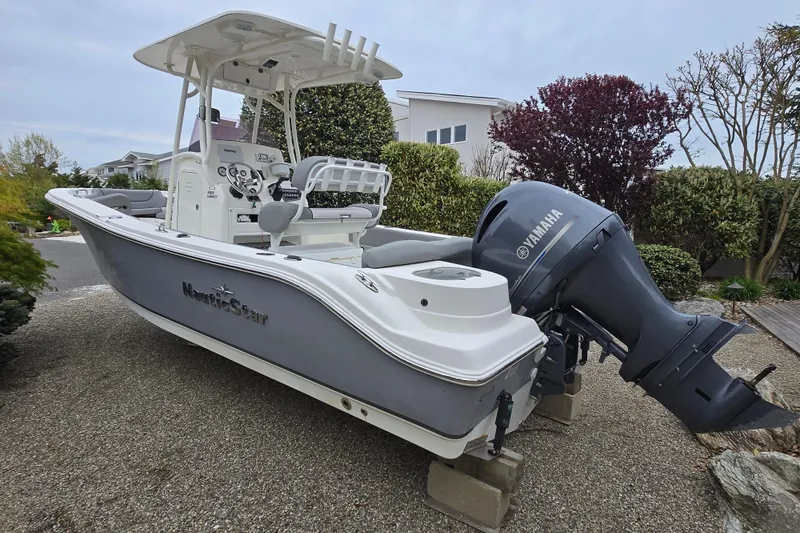 Slide: The Image of 2021 NauticStar 2302 Legacy boat with Yamaha engine, parked on gravel driveway. - 2