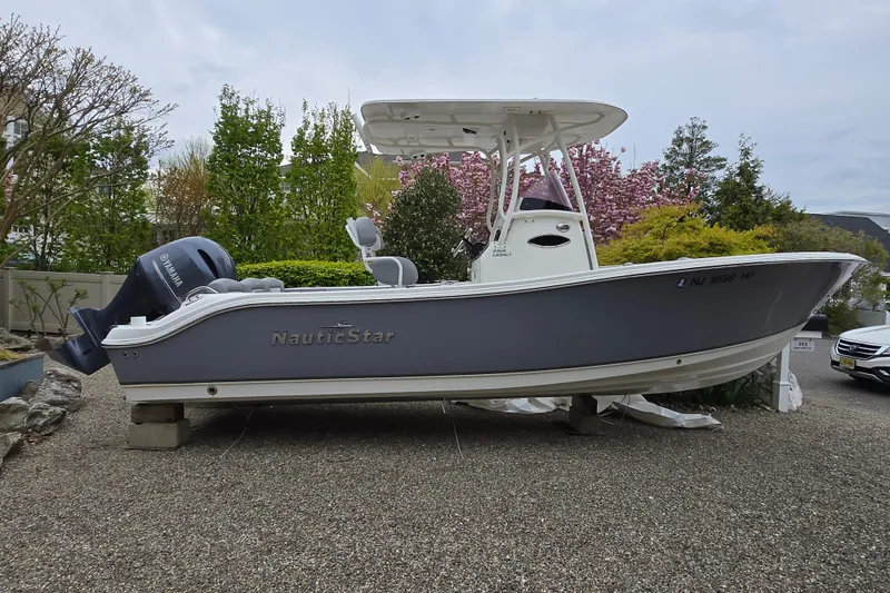 Slide: The Image of 2021 NauticStar 2302 Legacy boat on gravel, surrounded by trees and parked cars. - 22