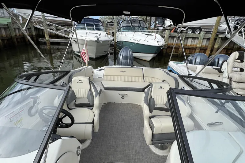 Slide: The Image of 2024 Stingray 211 DC boat interior with seating and steering wheel, docked at marina. - 23