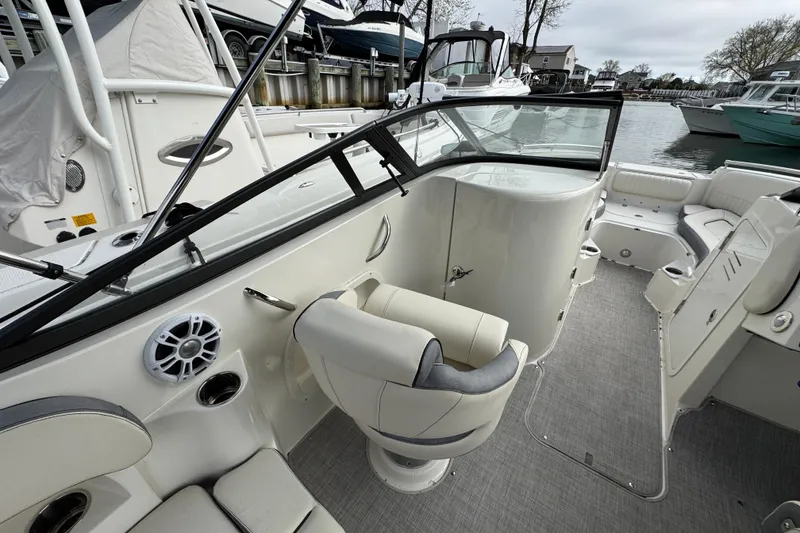 Slide: The Image of 2024 Stingray 211 DC boat interior with seating and steering console, docked near other boats. - 6