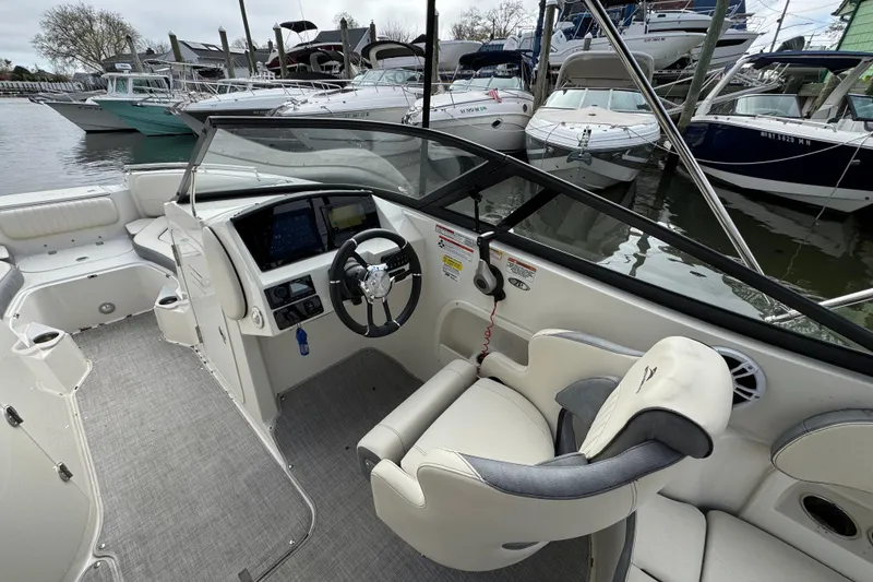Slide: The Image of 2024 Stingray 211 DC boat interior with steering wheel and dashboard, docked among other boats. - 7