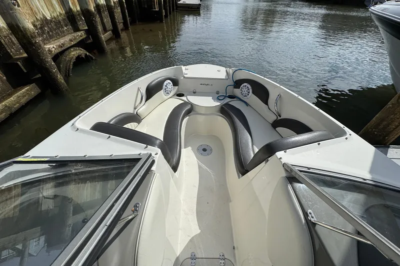 Slide: The Image of 2019 Stingray 204 LR boat interior with black and white seating, docked by wooden pilings. - 11