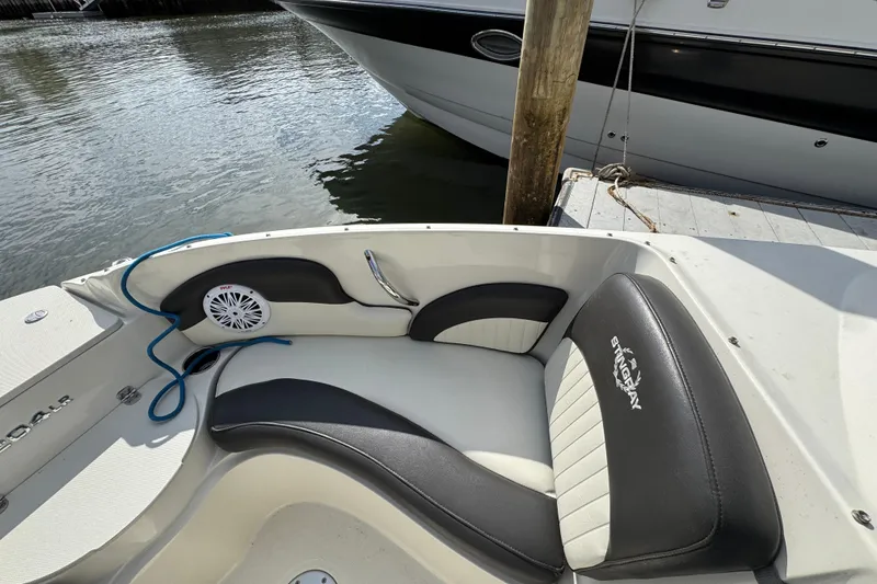 Slide: The Image of 2019 Stingray 204 LR boat interior with black and white seating, docked by water. - 13