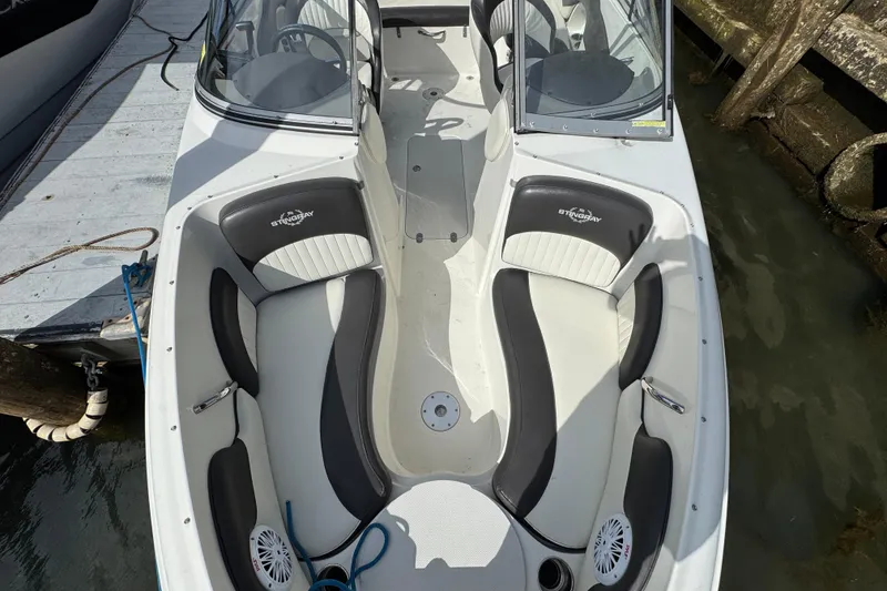 Slide: The Image of 2019 Stingray 204 LR boat interior with white and black seating, docked by the water. - 15