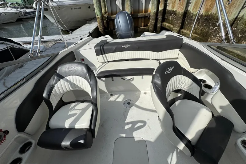 Slide: The Image of 2019 Stingray 204 LR boat interior with black and white seating, docked at marina. - 18