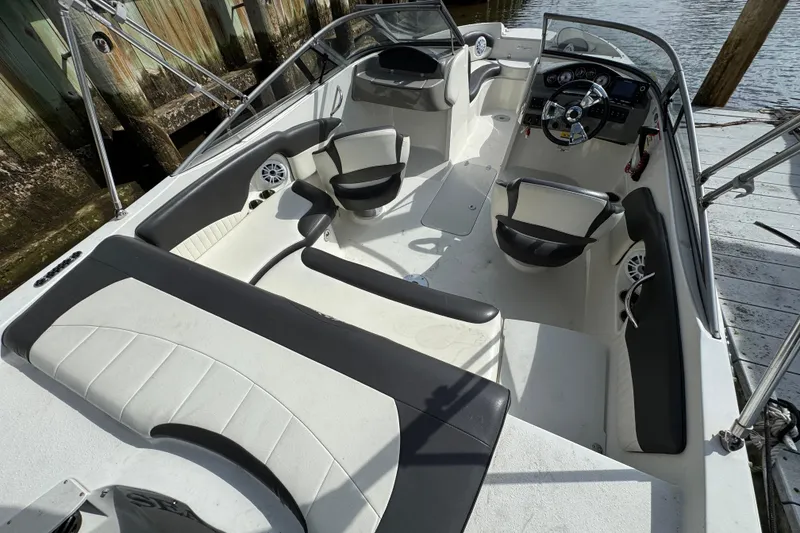 Slide: The Image of 2019 Stingray 204 LR boat interior with seating and steering wheel, docked by wooden posts. - 3