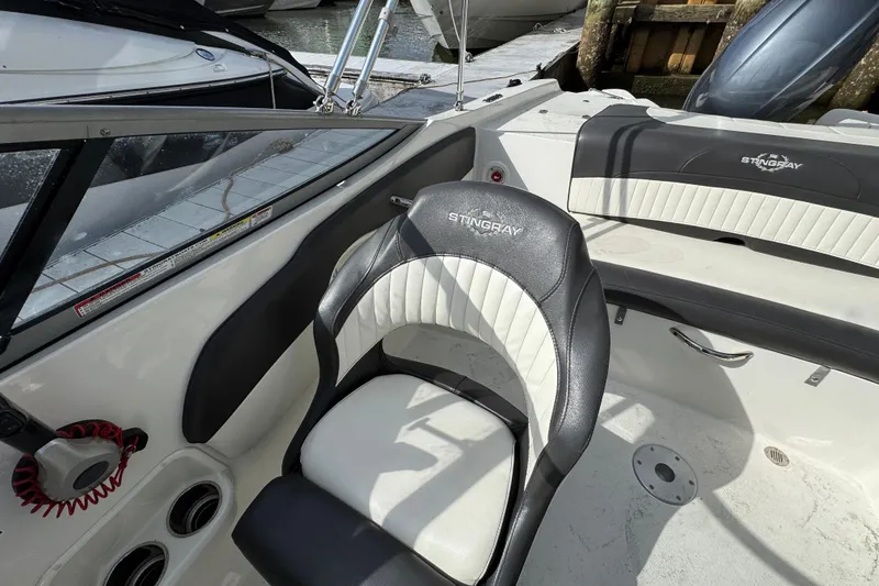 Slide: The Image of 2019 Stingray 204 LR boat interior with black and white seating, docked by the water. - 5