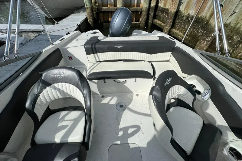 Slide: The Image of 2019 Stingray 204 LR boat interior with black and white seating, docked by wooden pier. - 6