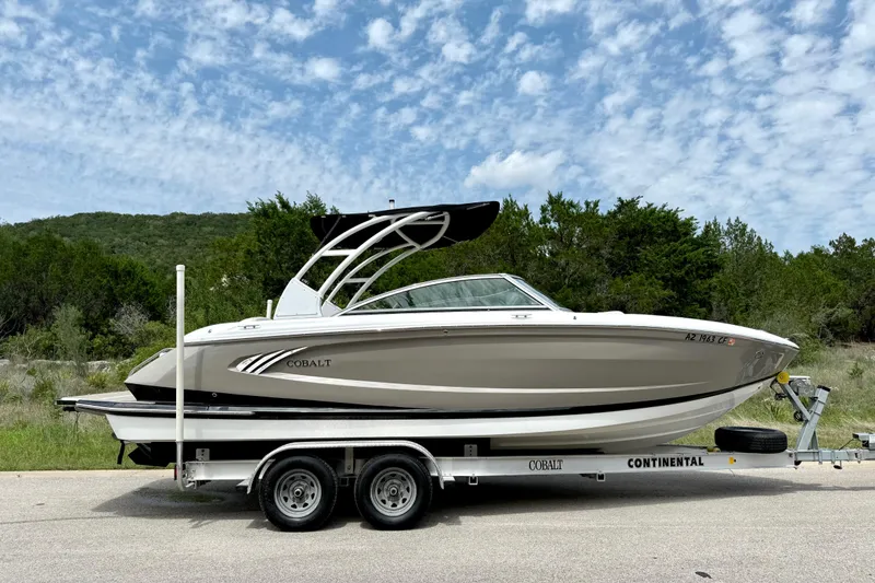 Slide: The Image of 2013 Cobalt A25 boat on trailer, parked on road with scenic background. - 13