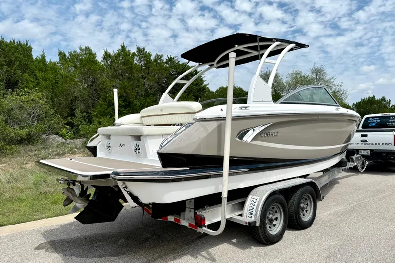 Slide: The Image of 2013 Cobalt A25 boat on trailer, parked outdoors with trees in background. - 14