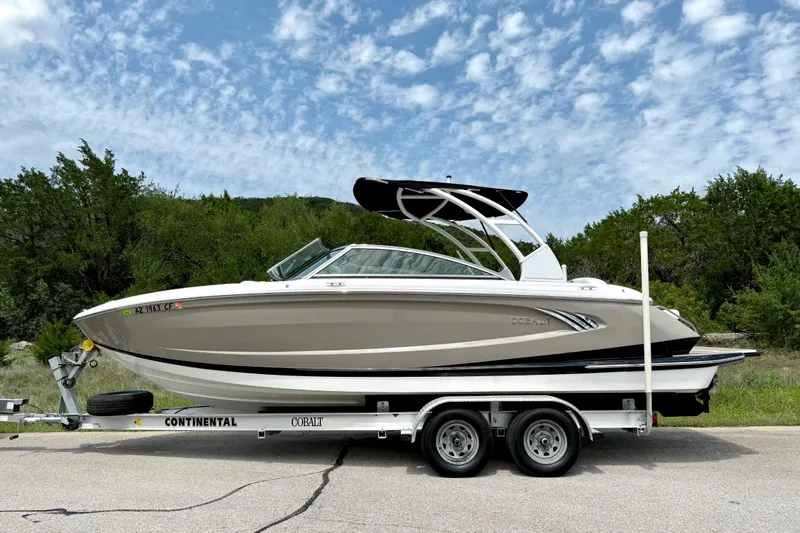 Slide: The Image of 2013 Cobalt A25 boat on trailer, parked on road with trees and cloudy sky background. - 17