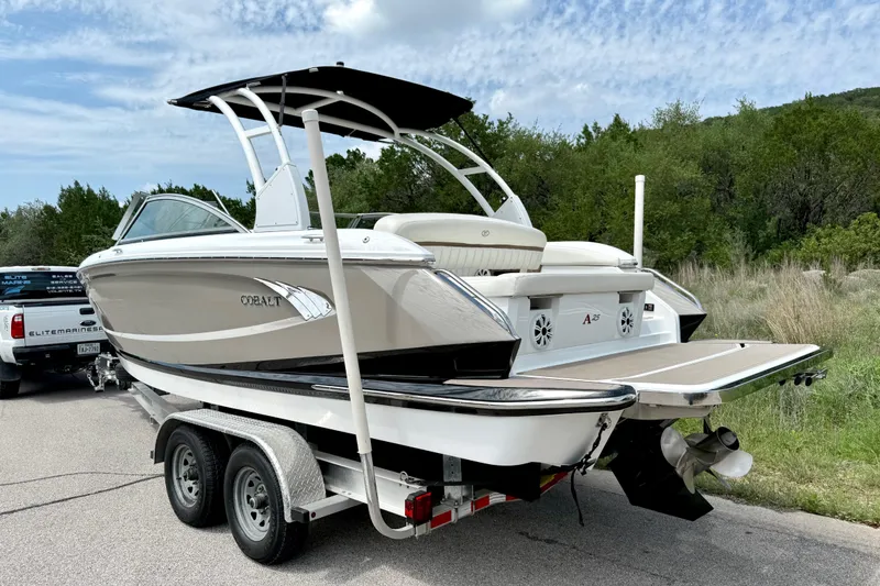 Slide: The Image of 2013 Cobalt A25 boat on trailer, parked outdoors with lush greenery background. - 18
