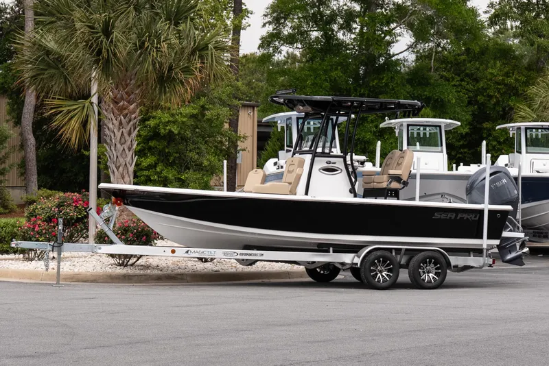 The Image of 2026 Sea Pro 230 Bay boat on trailer, parked near palm trees and greenery. - 1