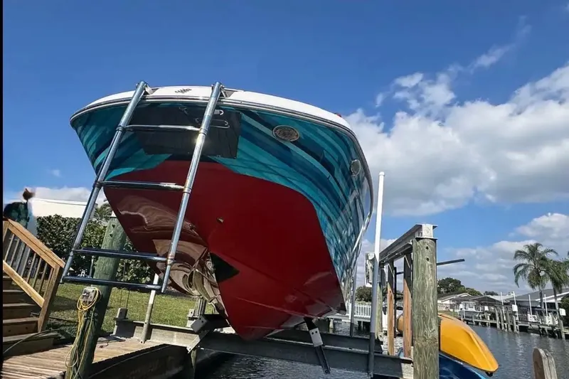 Slide: The Image of 2017 Four Winns HD240 boat on lift, vibrant red and blue hull, sunny day. - 5