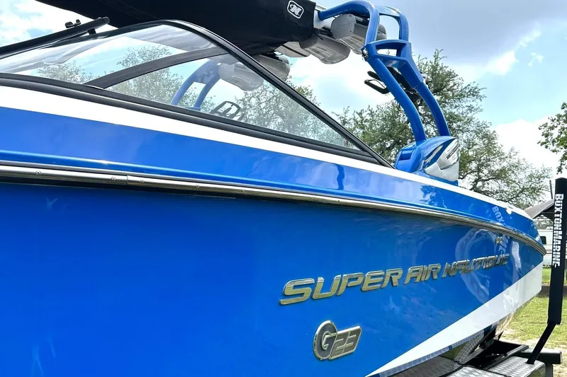 Slide: The Image of 2013 Nautique Super Air Nautique G23 boat in vibrant blue, docked outdoors. - 15