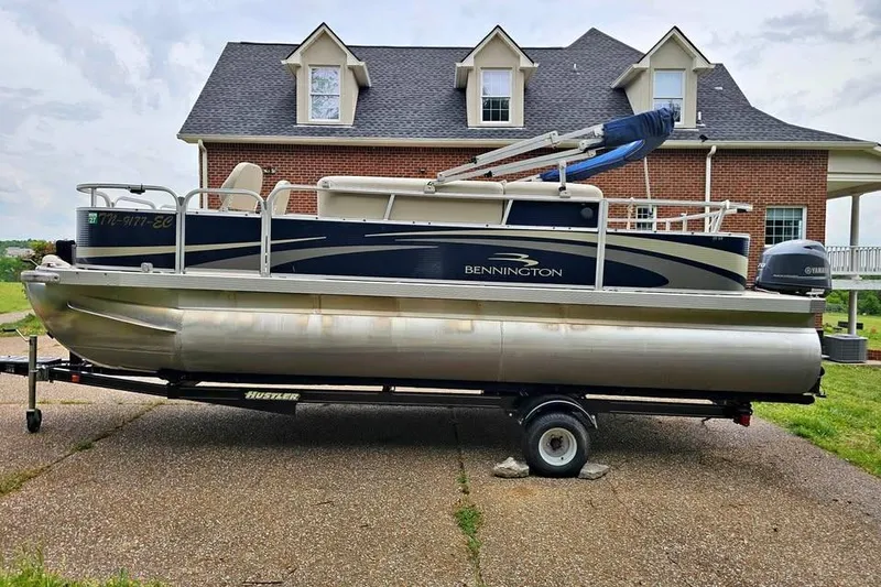 The Image of A 2012 Sweetwater 20sf pontoon boat on a trailer, parked in front of a brick house. - 0