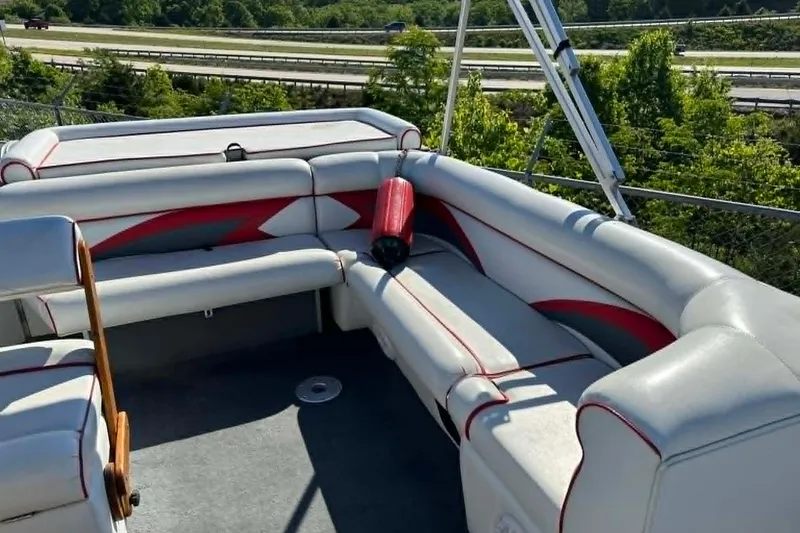 Slide: The Image of 1999 PlayCraft Sport 2400 boat interior with white and red seating, near highway and greenery. - 13