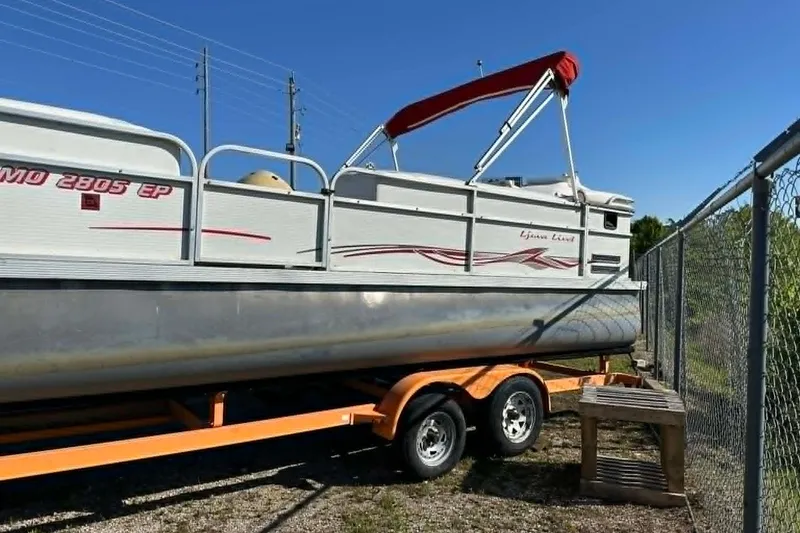 Slide: The Image of 1999 PlayCraft Sport 2400 pontoon boat on trailer, parked near a chain-link fence. - 17
