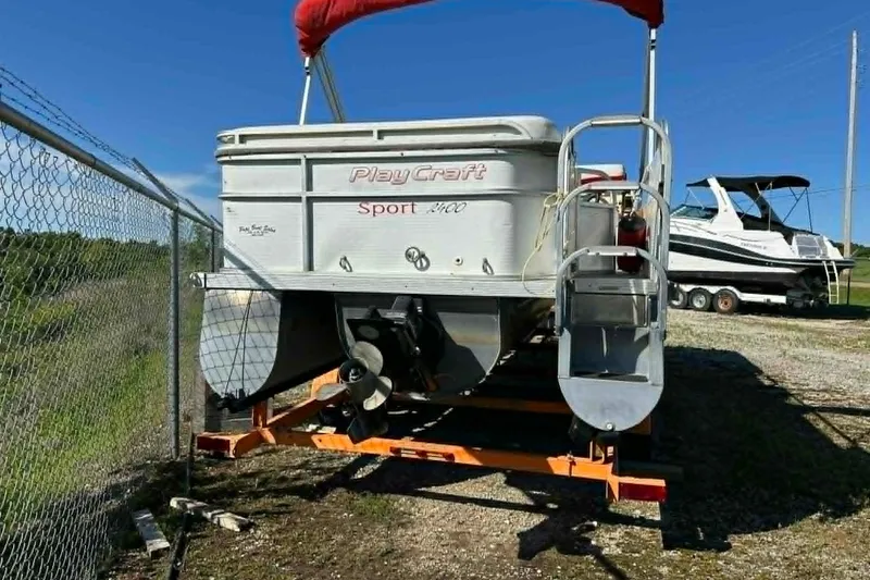 Slide: The Image of 1999 PlayCraft Sport 2400 pontoon boat on trailer, parked near a fence. - 4