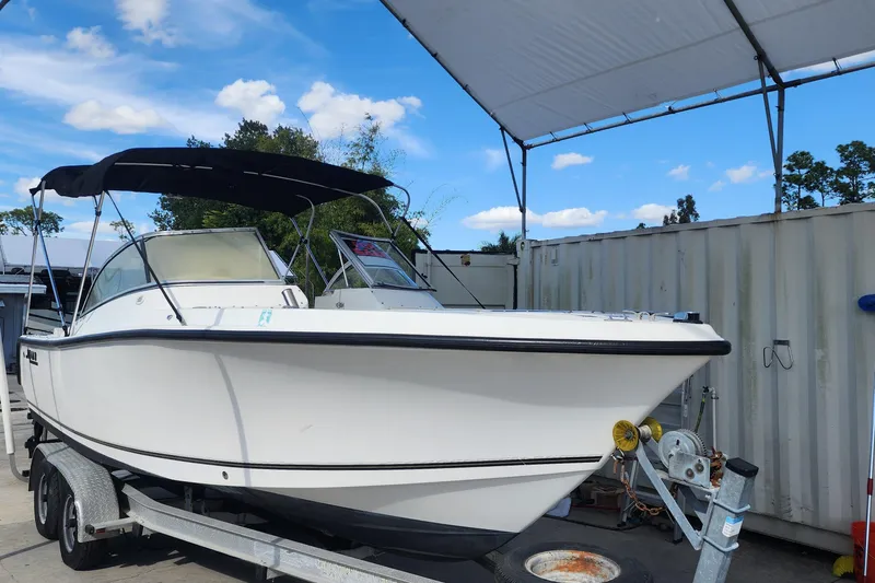 Slide: The Image of 2006 Mako 216 Dual Console boat on trailer under canopy, clear sky background. - 16