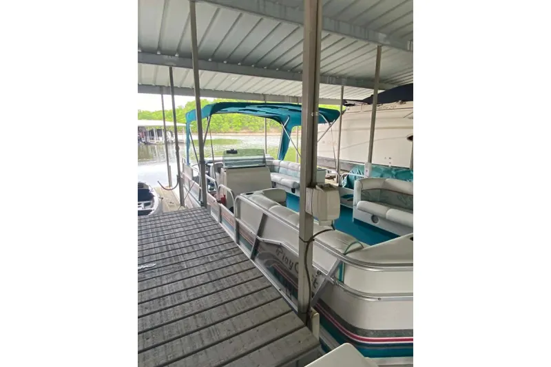 Slide: The Image of 1995 PlayCraft Powertoon 26 pontoon boat docked under a covered marina. - 11
