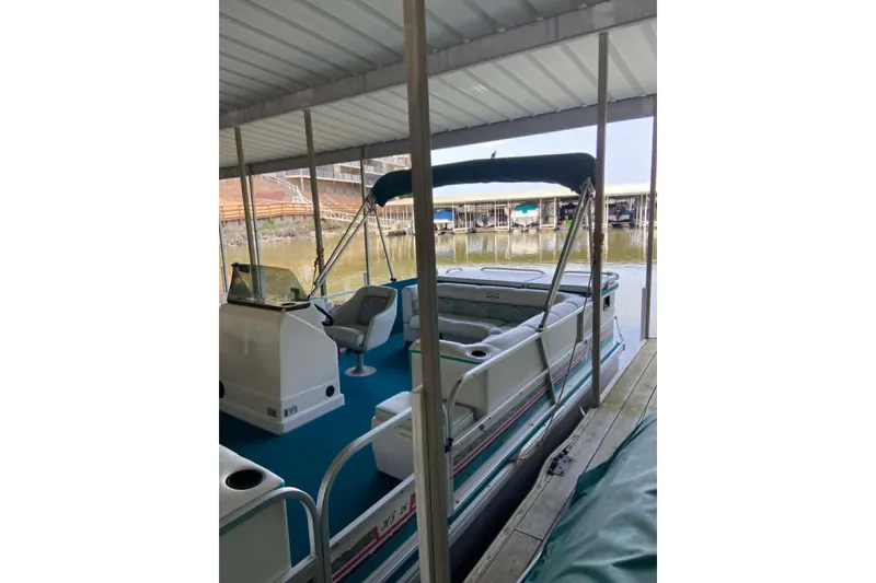 Slide: The Image of 1995 PlayCraft Powertoon 26 pontoon boat docked under a covered marina. - 16