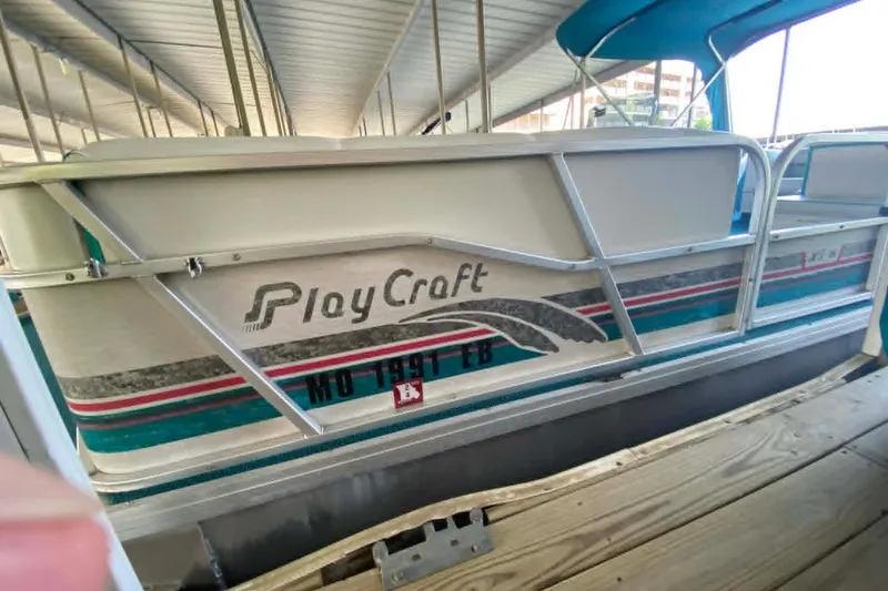 Slide: The Image of 1995 PlayCraft Powertoon 26 pontoon boat docked under a covered marina. - 4