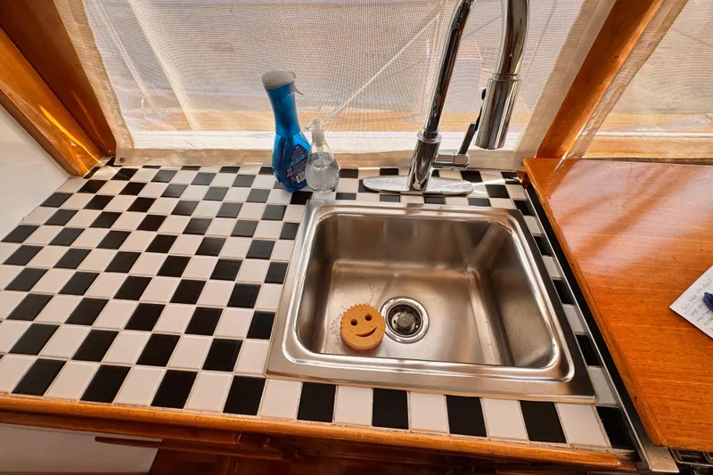 Slide: The Image of 1978 Roughwater 41 boat kitchen sink with checkered countertop and cleaning supplies. - 19