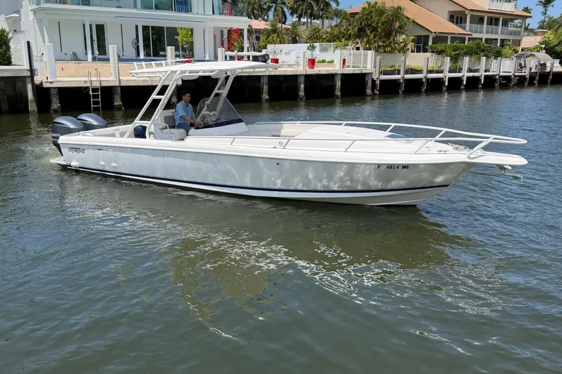The Image of 2003 Intrepid 323 Cuddy boat cruising on a sunny waterfront near luxury homes. - 0