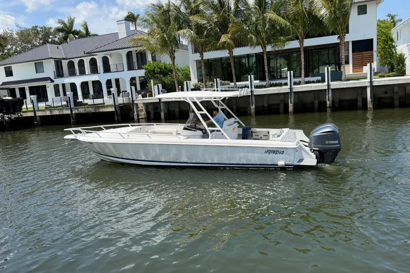Slide: The Image of 2003 Intrepid 323 Cuddy boat cruising near waterfront homes with palm trees. - 1