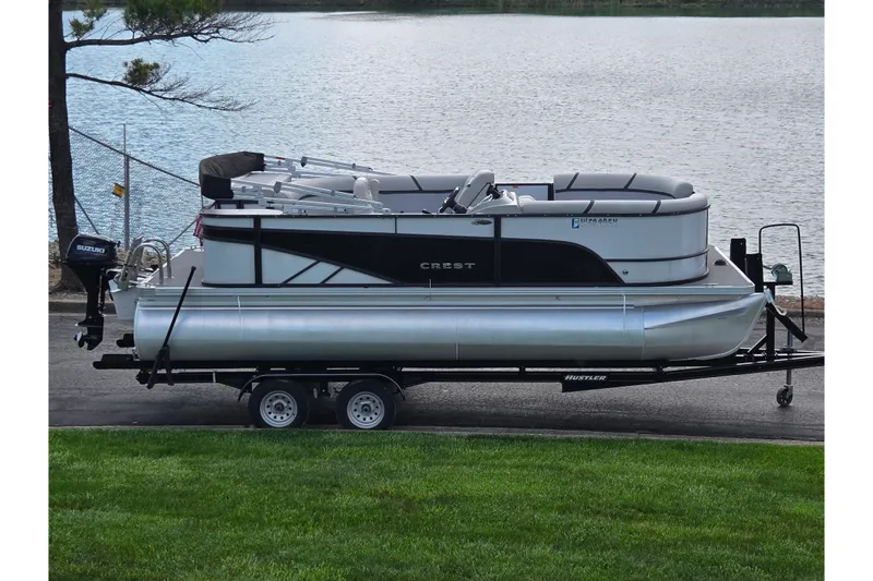The Image of 2023 Crest Classic LX 200 pontoon boat on trailer by a lake. - 0