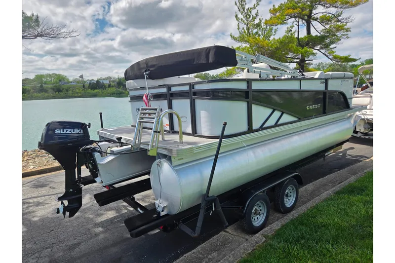 Slide: The Image of 2023 Crest Classic LX 200 pontoon boat on trailer by a lake. - 1