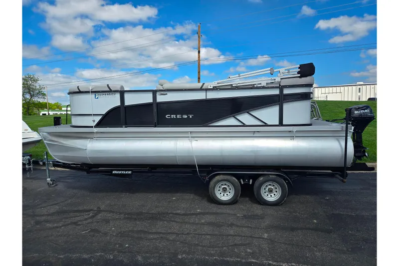 Slide: The Image of 2023 Crest Classic LX 200 pontoon boat on trailer, parked outdoors under blue sky. - 4