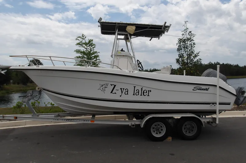 The Image of 2002 Seaswirl Striper 2101 Center Console boat on trailer, parked near a lake. - 0