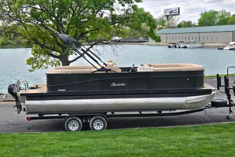 The Image of 2021 Barletta C22QC pontoon boat on trailer by a lakeside with trees. - 0