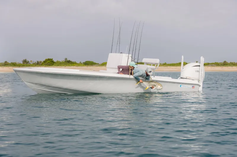 Slide: The Image of 2026 Contender 24 Bay boat on water, person releasing fish, scenic shoreline background. - 6