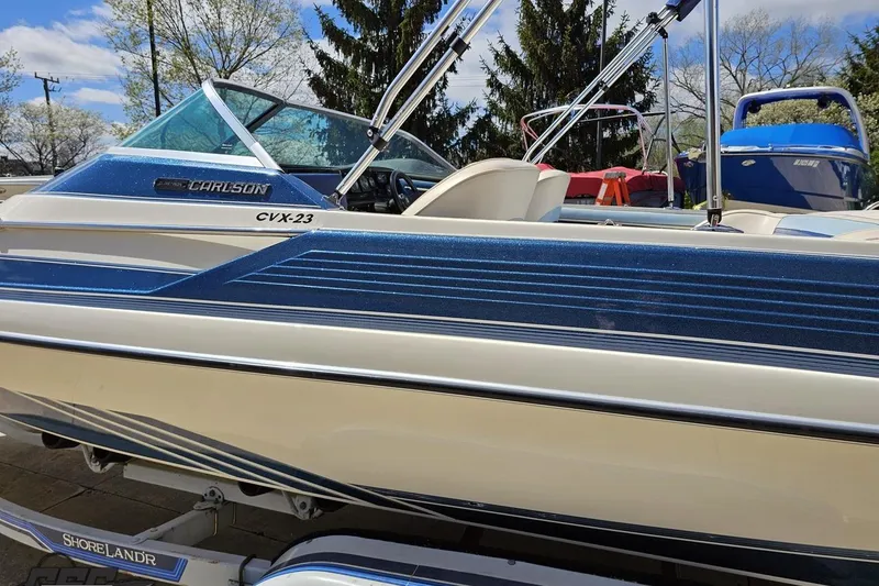 Slide: The Image of 1988 Glastron/Carlson CVX-23 boat with blue and white design, parked on trailer. - 19