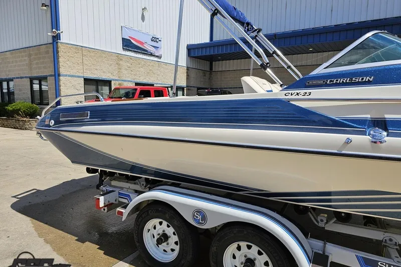 Slide: The Image of 1988 Glastron/Carlson CVX-23 boat on trailer, blue and white design, parked outside a building. - 4