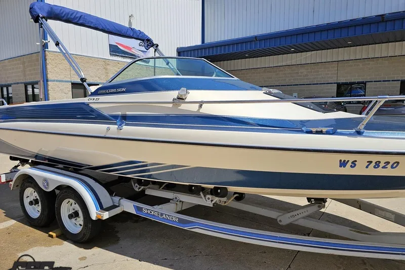 Slide: The Image of 1988 Glastron/Carlson CVX-23 boat on trailer, blue and white design, parked outside a building. - 7