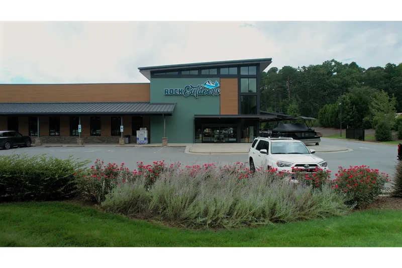 Slide: The Image of Modern building with "Rock Outdoors" sign, surrounded by greenery, featuring a white SUV in the foreground. - 9